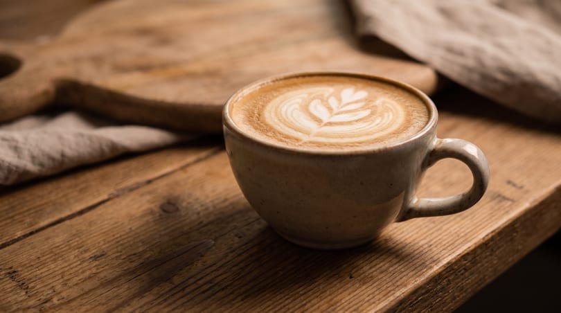 A latte with intricate leaf art in a ceramic mug on a rustic wooden table.